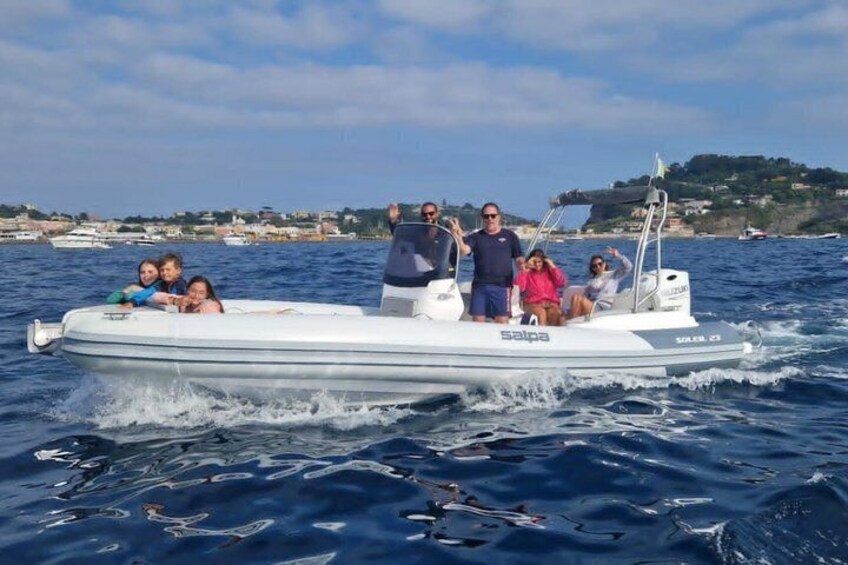 A group of people on a small motorboat with 'Salpa' written on the side, moving on a body of water with a coastline in the background. 1
