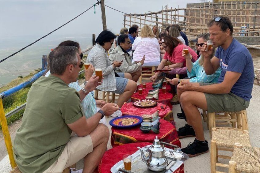 A group of people sitting at a table outdoors, eating and drinking. 5
