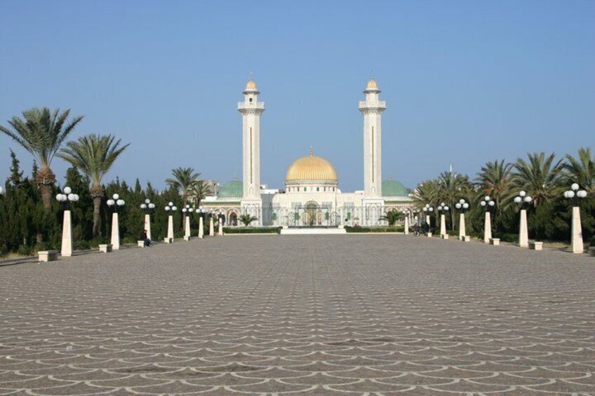 A mosque with two minarets and a golden dome, surrounded by palm trees and a paved walkway. 5