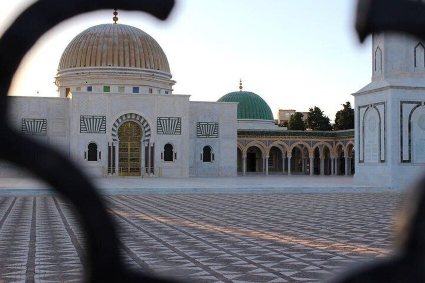 A mosque with a large dome, a green dome, and a courtyard with patterned tiles. 4