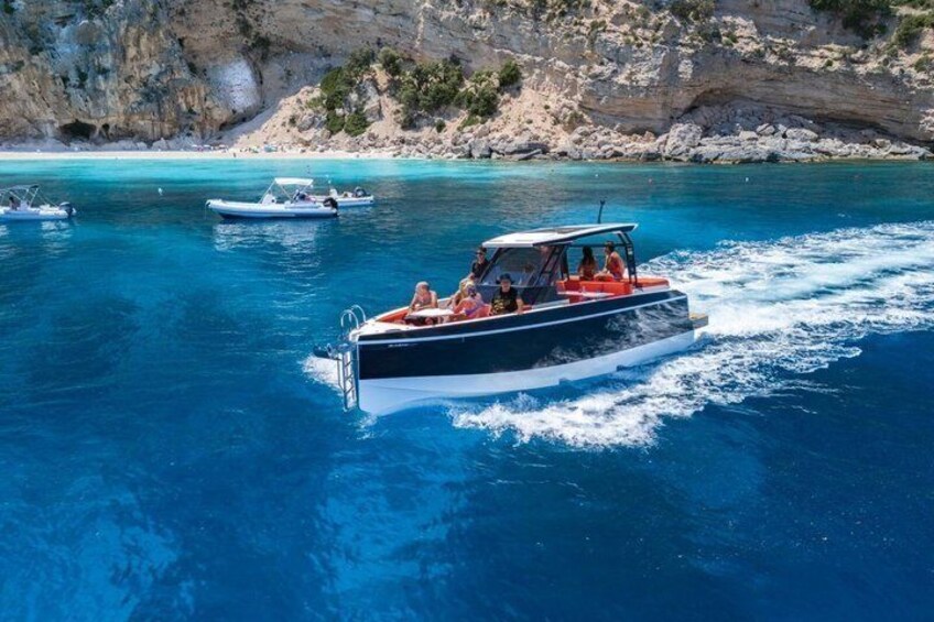 A boat with passengers on a clear blue sea, rocky cliffs in the background. 1
