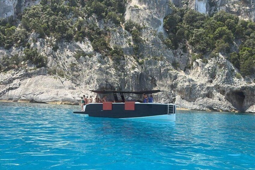 A boat with people on a clear blue sea, surrounded by rocky cliffs and greenery. 2