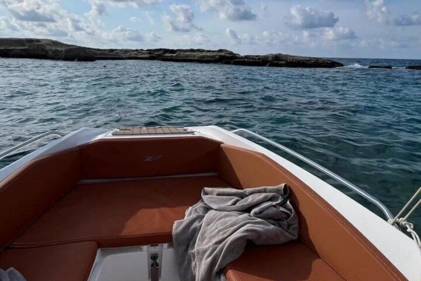 A boat with a brown interior and a white exterior, floating on calm water with rocky land in the distance. 4