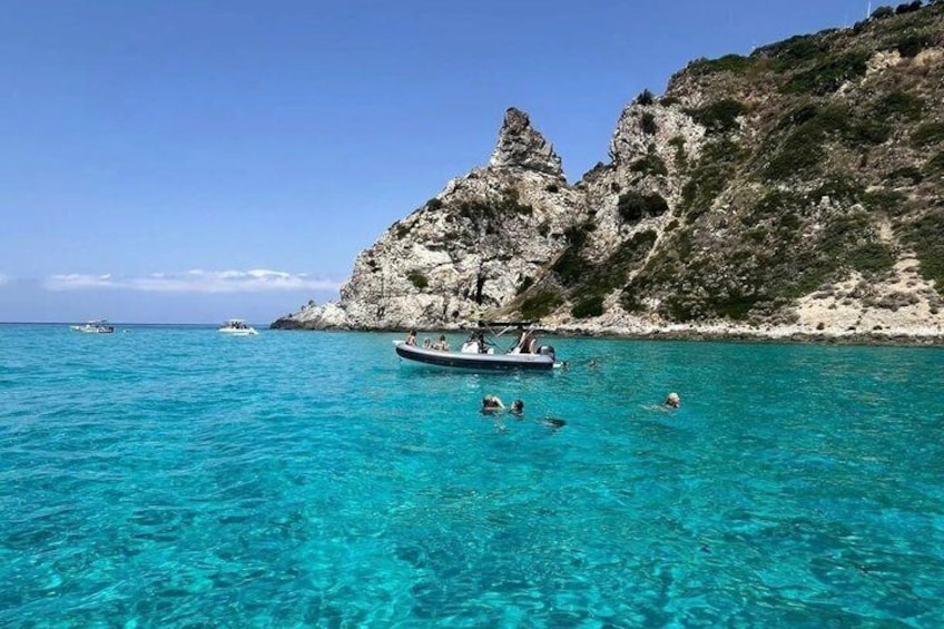 A boat on turquoise water, swimmers, and rocky cliffs. 1