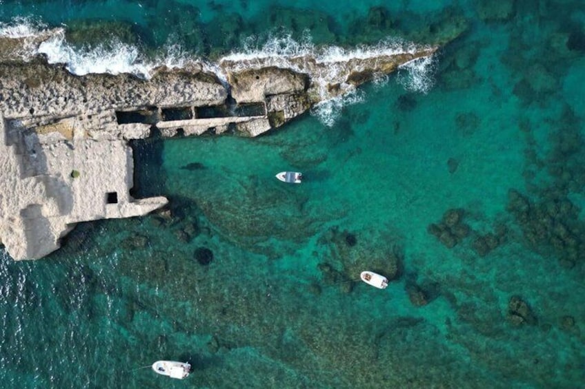 An aerial view of a coastal area with clear turquoise waters, rocky cliffs, and several boats anchored near the shore. 2