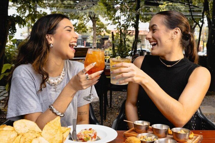 Two people toasting with drinks at an outdoor table with food and drinks. 1