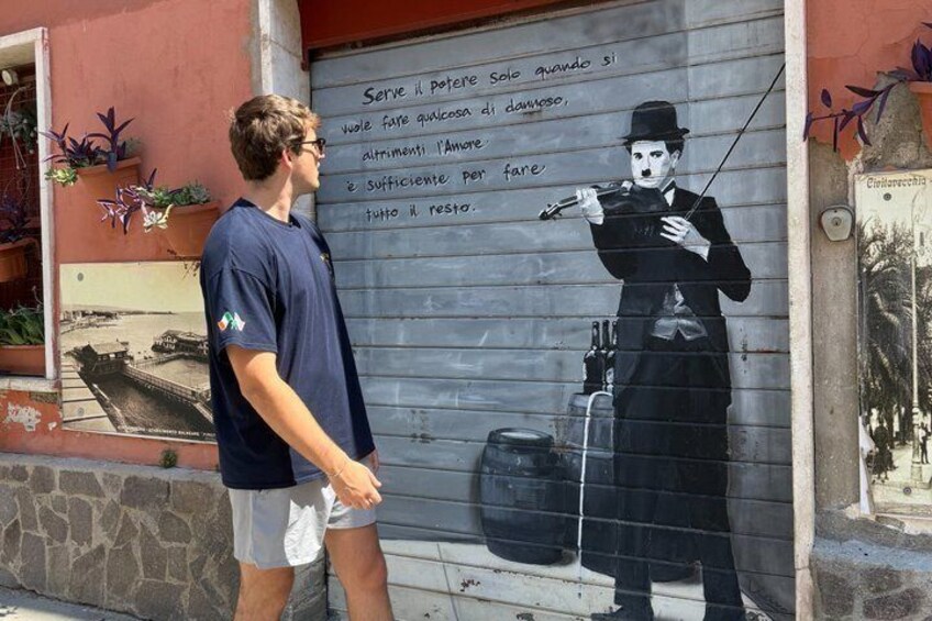 A mural of a man with a bowler hat and a violin, standing next to a wall with text in Italian. 4