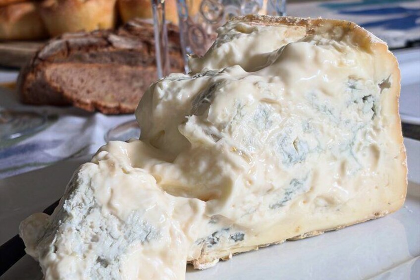 A piece of blue cheese with a creamy white rind, accompanied by a slice of bread and a glass of white wine on a table. 4