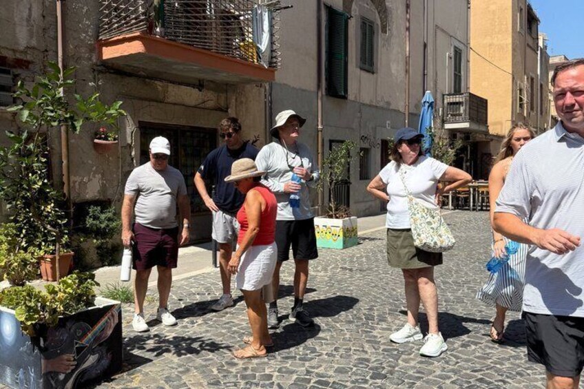 A cobblestone street with people walking, buildings, and potted plants. 5