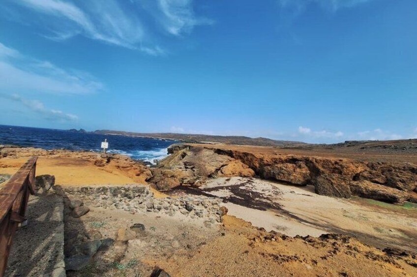 A coastal landscape with rocky terrain, a wooden walkway, and a white sign. 4