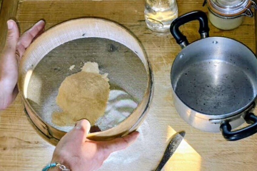 A hand holding a bowl with a piece of dough, a pot, and a knife on a wooden surface. 2