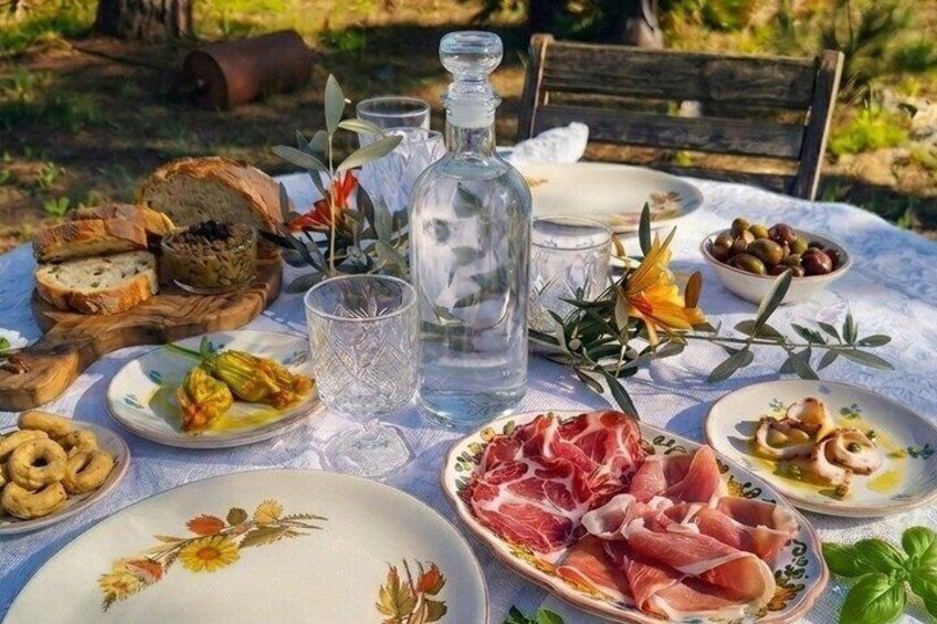 An outdoor picnic with bread, olives, cheese, and cured meats on a table. 3
