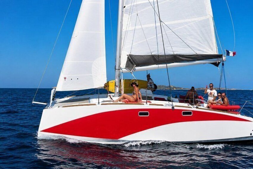 A red and white sailboat on the water with people on deck. 1