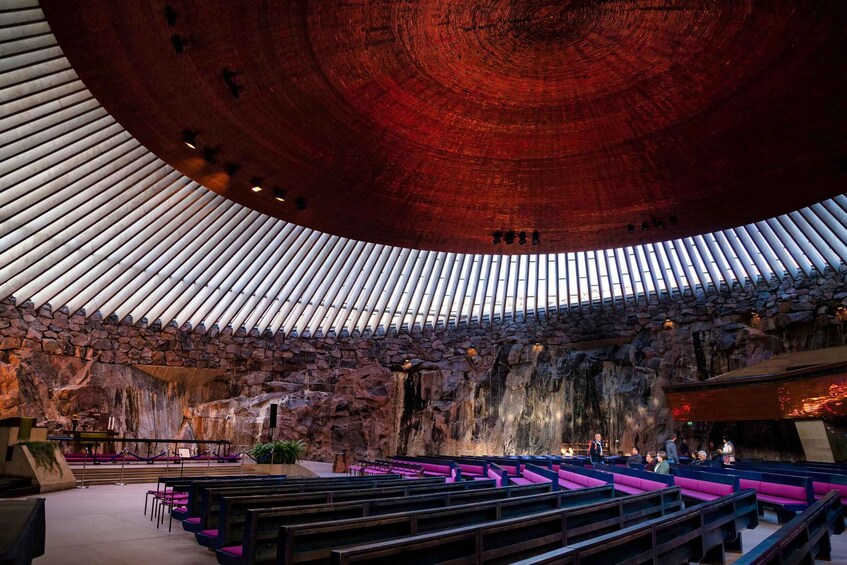 A large hall with a curved ceiling, stone walls, and rows of purple and blue seating. 1