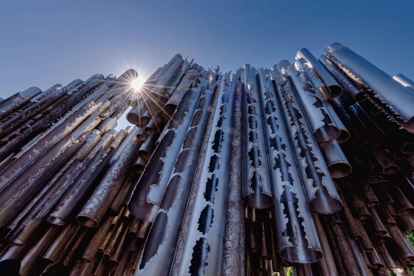A large collection of cylindrical metal pipes with cutouts, arranged in a pyramid-like structure, under a clear sky. 2