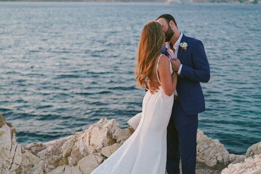 A couple embracing by a rocky shoreline with a body of water in the background. 5