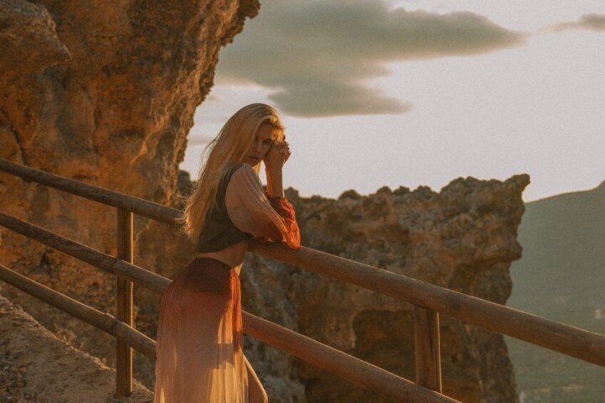 A person standing on a rocky outcrop with a railing, overlooking a mountainous landscape. 1