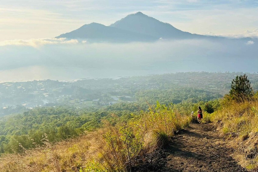 A hiker on a mountain trail with a view of a volcano and a valley below. 4
