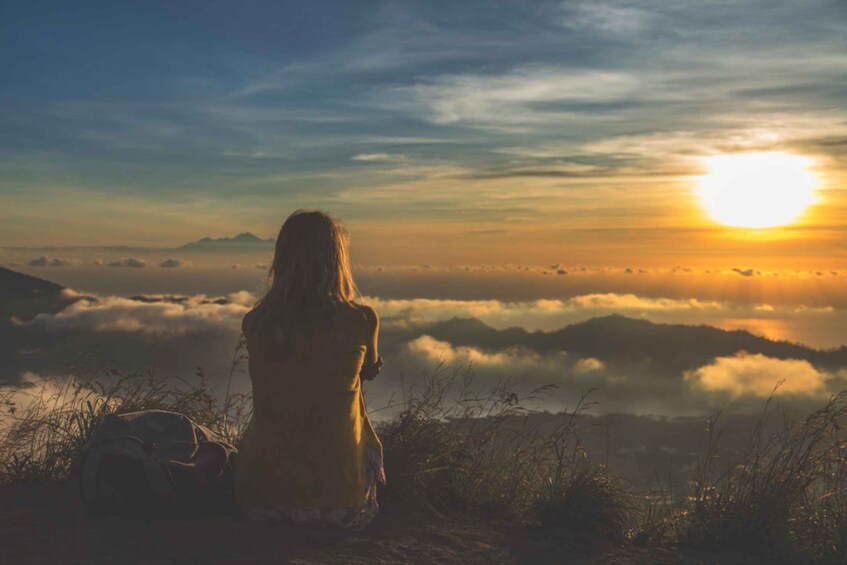 A person sitting on a hill overlooking a valley with a sunrise or sunset. 1