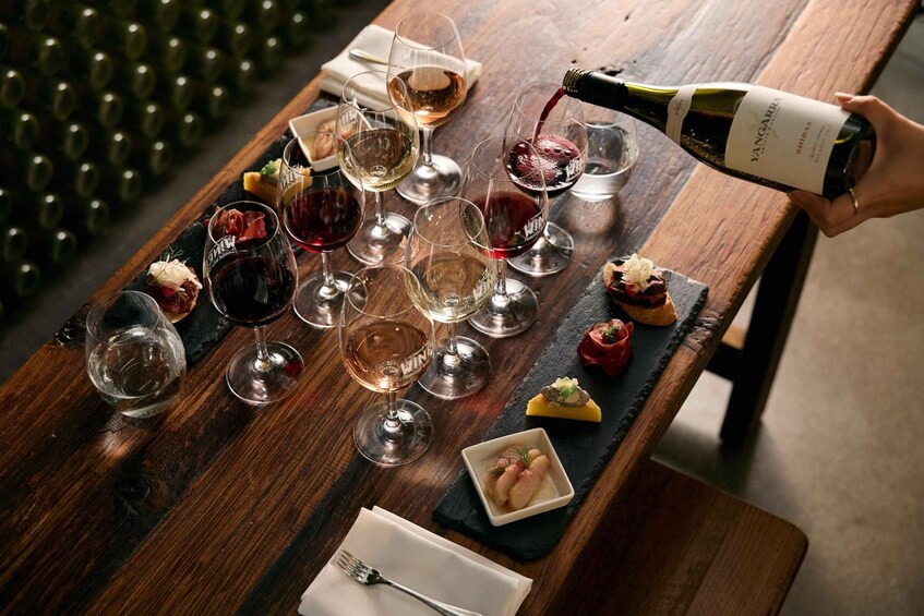A wooden table with wine glasses, a bottle of wine being poured, and small dishes of food. 1