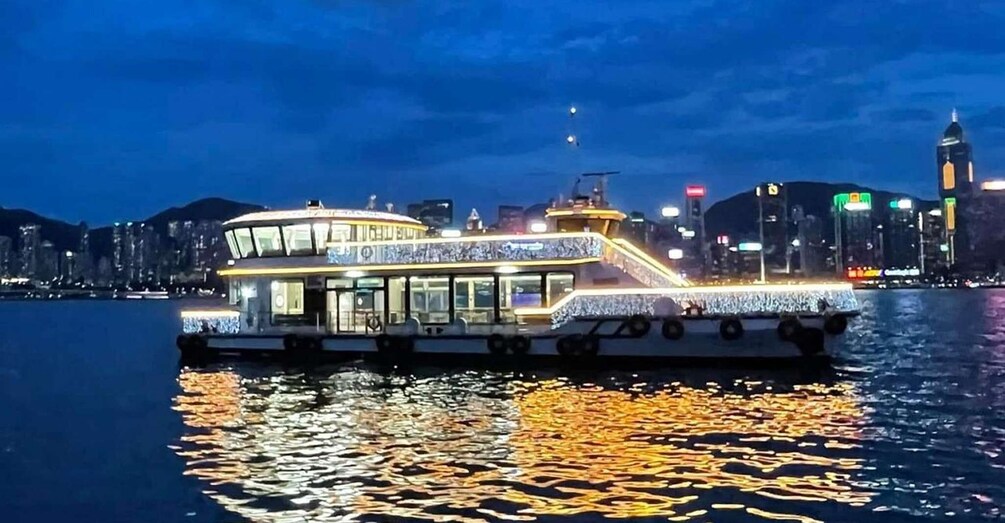 A brightly lit boat with a covered upper deck, docked at a waterfront with a city skyline in the background. 3