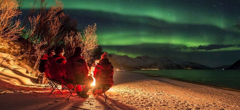 People sitting on chairs by a snowy beach, gazing at the northern lights. 5