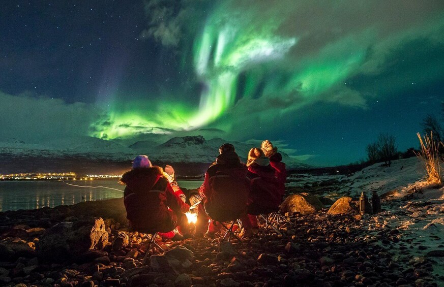 A group of people camping by a lake at night, watching the northern lights. 2