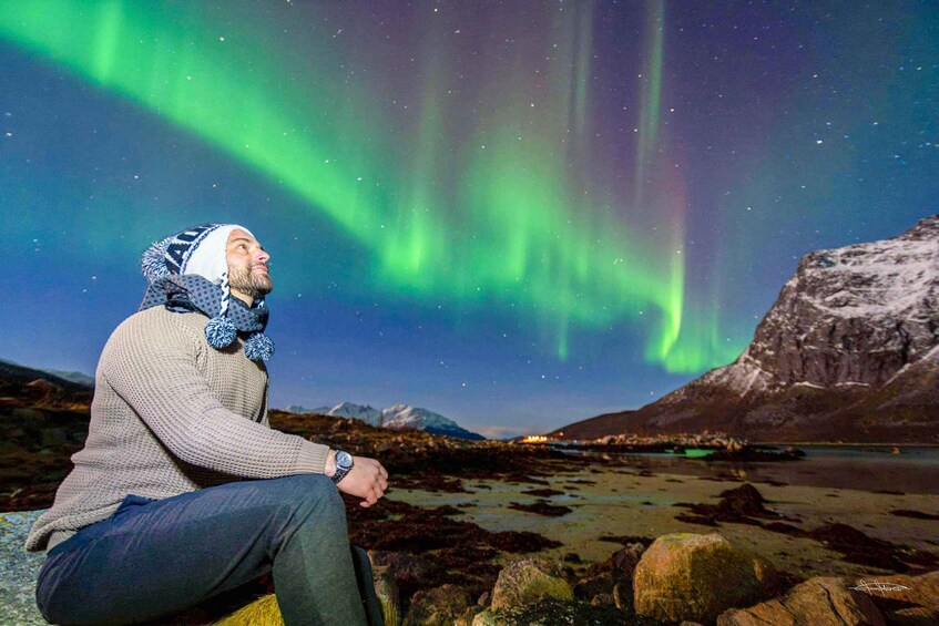 A person sitting on a rock, gazing at the northern lights. 1