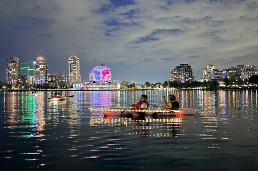 A nighttime cityscape with illuminated buildings and a large, colorful spherical structure in the distance. 2