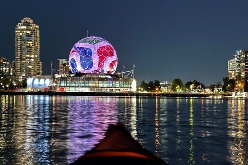 A nighttime cityscape with a brightly lit spherical structure reflecting on the water. 1