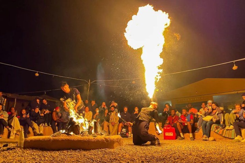 A nighttime outdoor event with a large fire display, a crowd of people, and a person performing a fire act. 2
