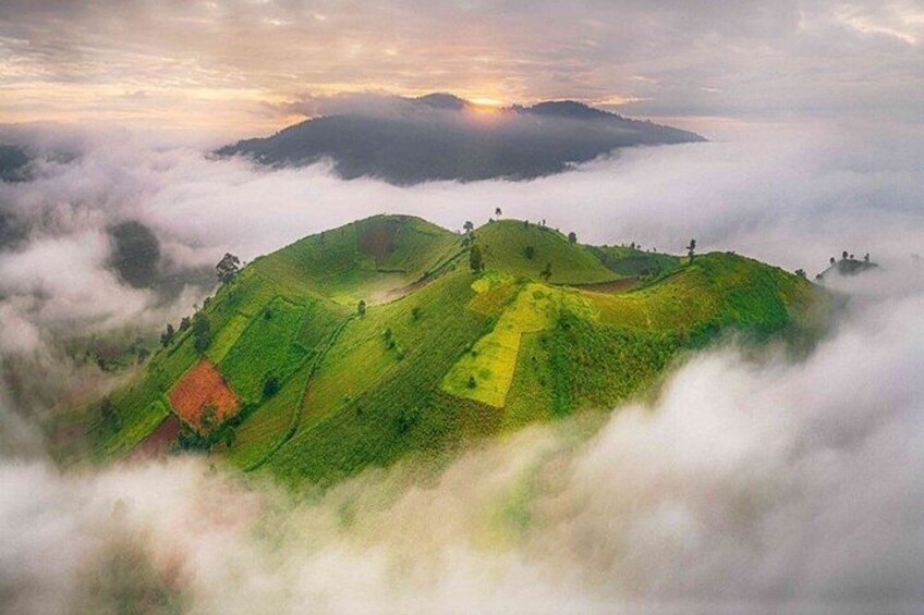 A landscape of rolling hills with a sunrise or sunset in the background, surrounded by clouds. 1