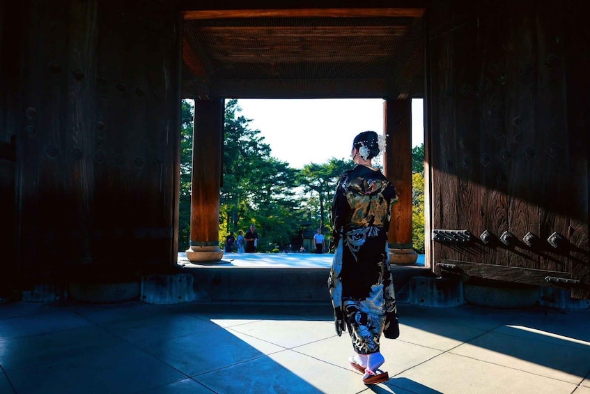 A person in traditional attire walking through a wooden structure with a view of a park. 4