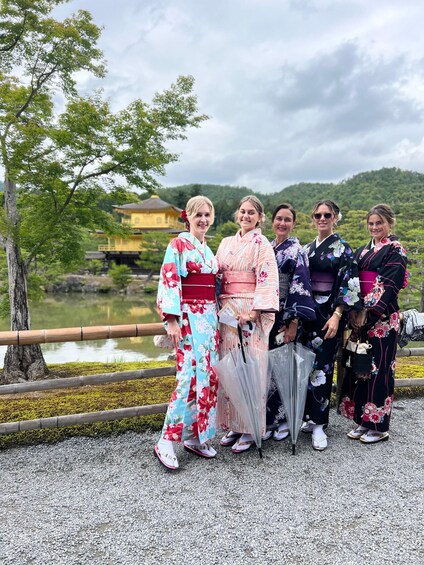 A group of people in traditional Japanese kimonos standing by a pond with a temple in the background. 1