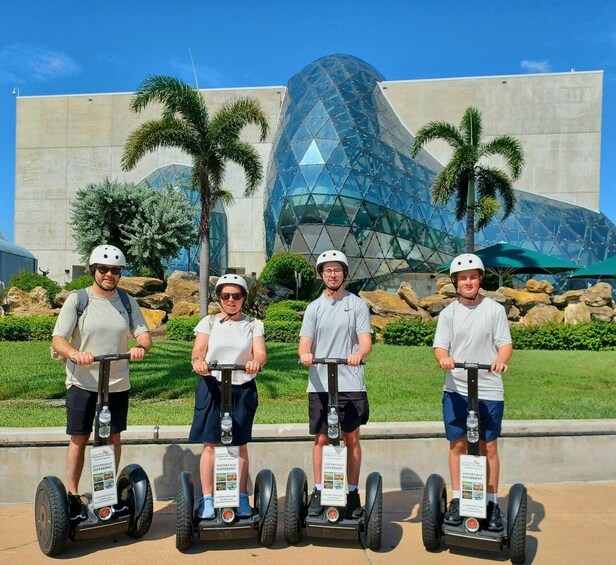 Four people on segways in front of a modern glass building. 4