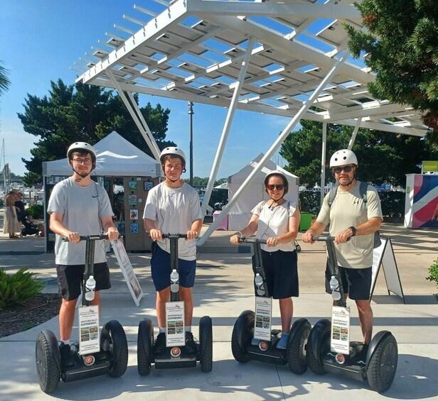 Four people riding segways in an outdoor setting with a white structure overhead. 5
