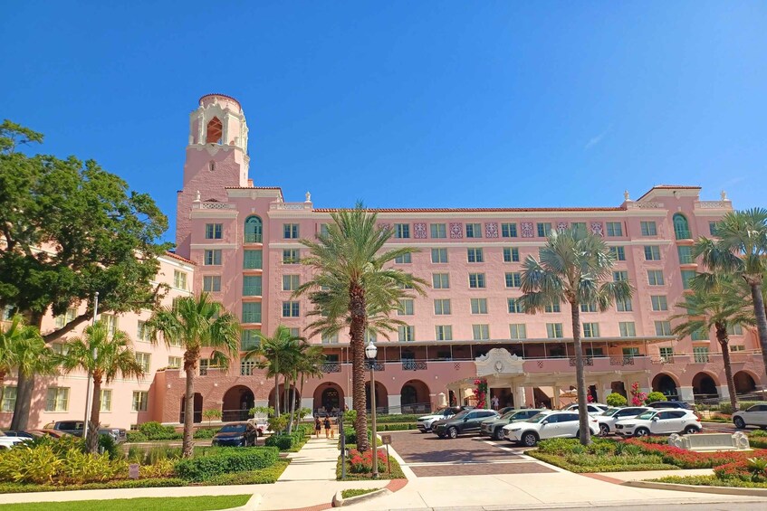A pink building with a tower, palm trees, and parked cars. 2