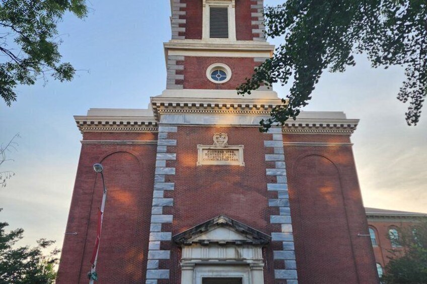 A brick church with a clock tower, a plaque, and a door. 4