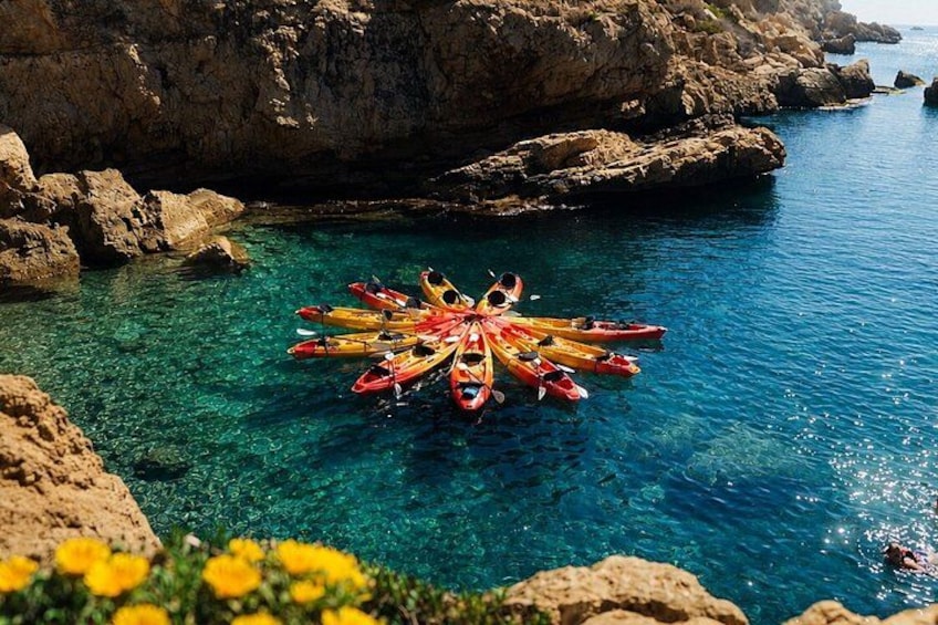 Kayaks arranged in a circle on clear water near rocky cliffs. 4