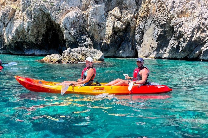 Two people kayaking on a clear turquoise water body with rocky cliffs in the background. 5