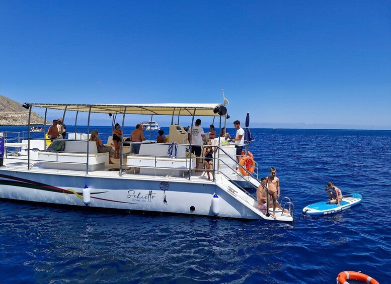 A boat with people on board, some standing and some sitting, with a clear blue sky and calm sea in the background. 5
