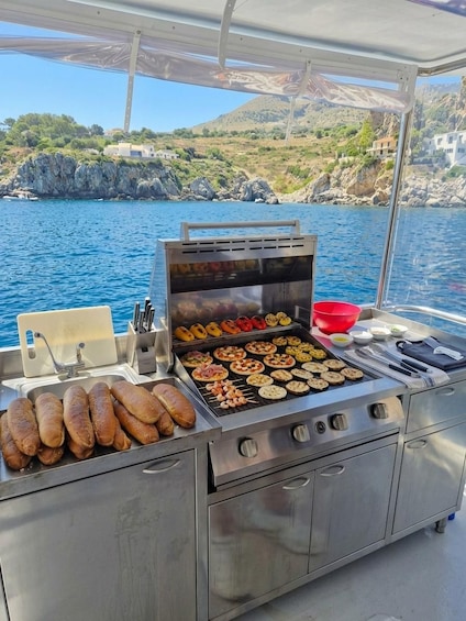 A stainless steel grill with sausages and grilled vegetables on a boat. 2