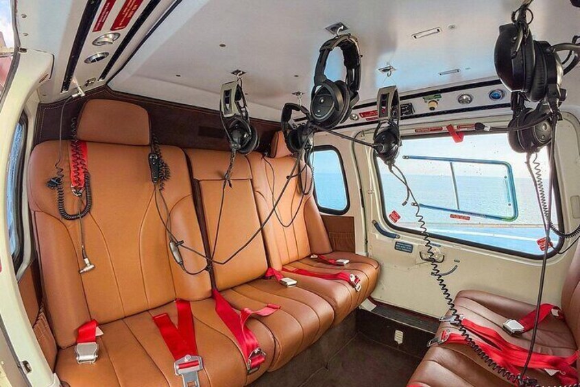 A cabin interior with leather seats, red safety belts, and headphones hanging from the ceiling. 5