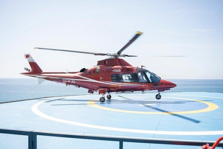 A red helicopter with 'ICARJ' on its tail, parked on a blue deck with yellow and white markings. 3