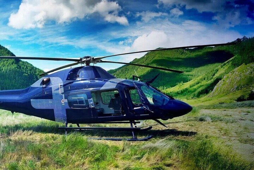 A helicopter parked on a grassy field with a mountainous backdrop. 2