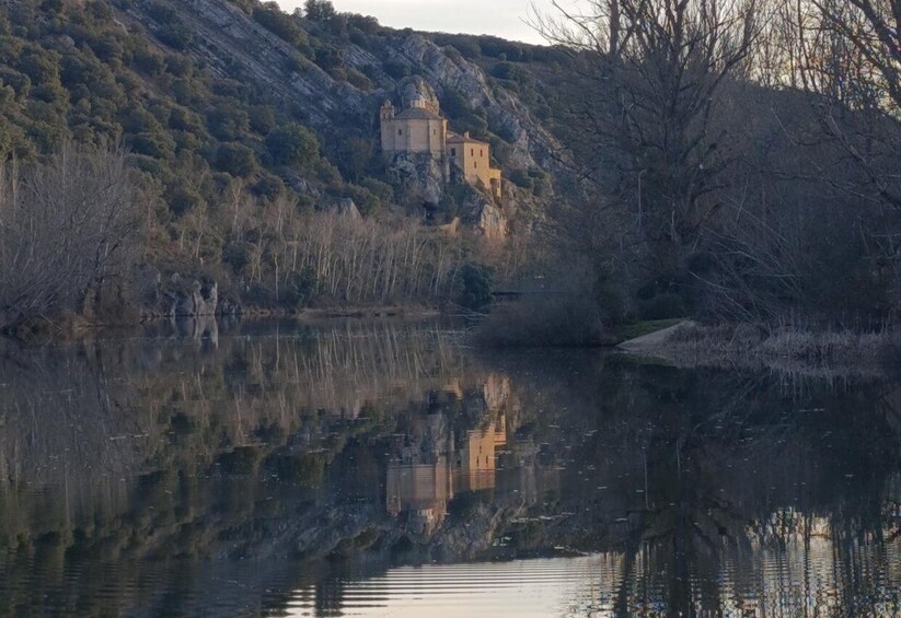 A serene lake with a castle on a hill, surrounded by trees and rocky terrain. 1