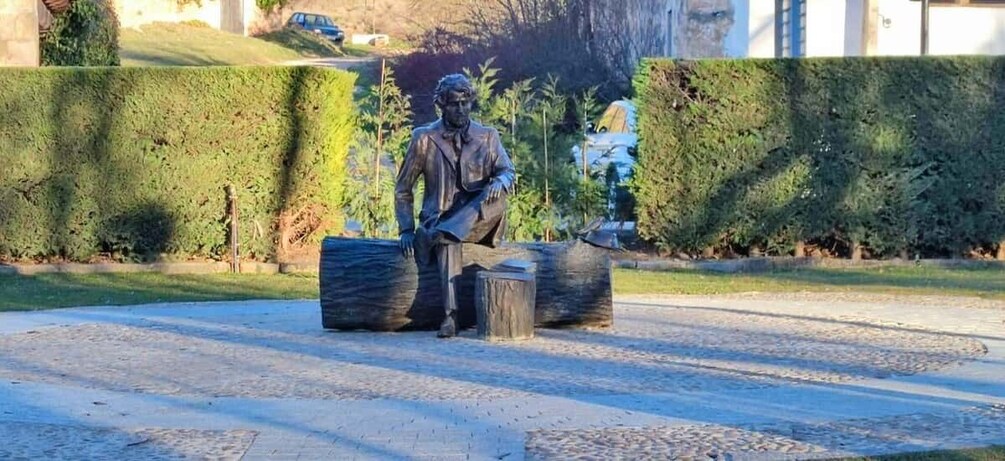 A statue of a man sitting on a log with a suitcase beside him. 2
