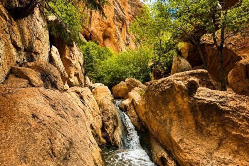 A canyon with a waterfall, large boulders, and green vegetation. 3
