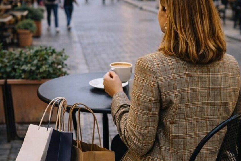 A person sitting at a table with a cup and shopping bags. 2