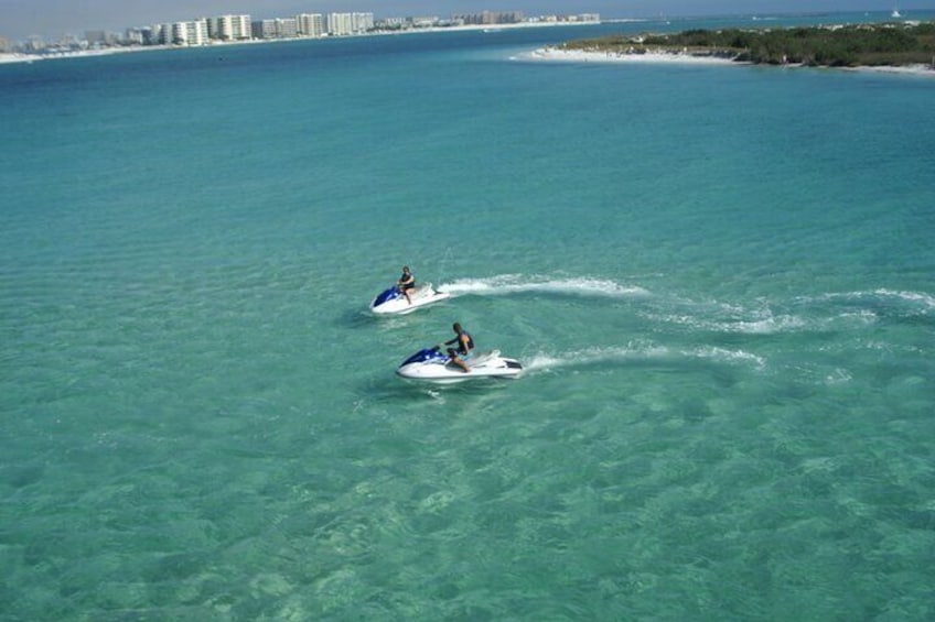 Two jet skis on a clear turquoise sea with a distant shoreline and buildings. 3